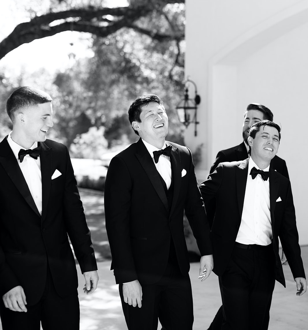 The groom smiles and laughs while walking with his groomsmen outside before his wedding.