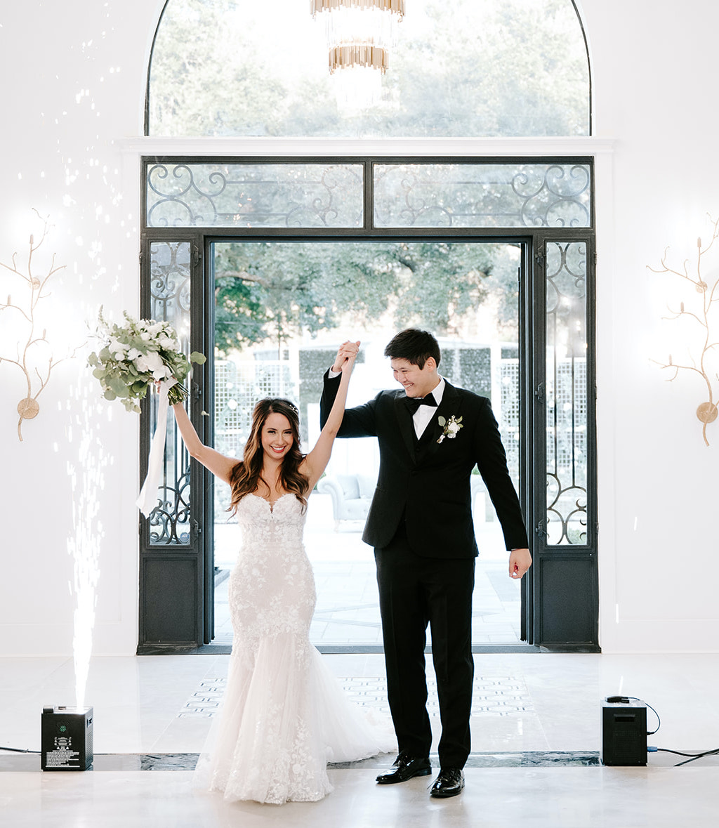 The bride and groom enter the reception room and the bride holds up her bridal bouquet.