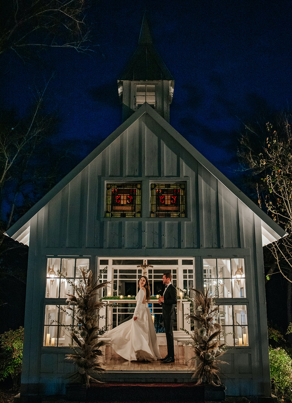 A bride and groom dance at dusk in a small white chapel that is lit up inside at 7F Lodge in Aggieland.