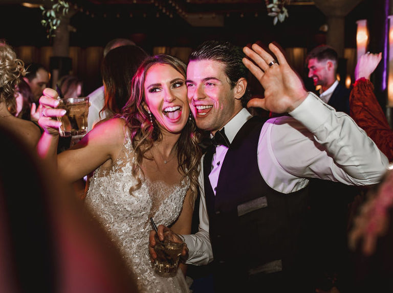 The bride and groom hold drinks in their hands at their wedding reception where they celebrate their love story at The Astorian in Houston, TX.