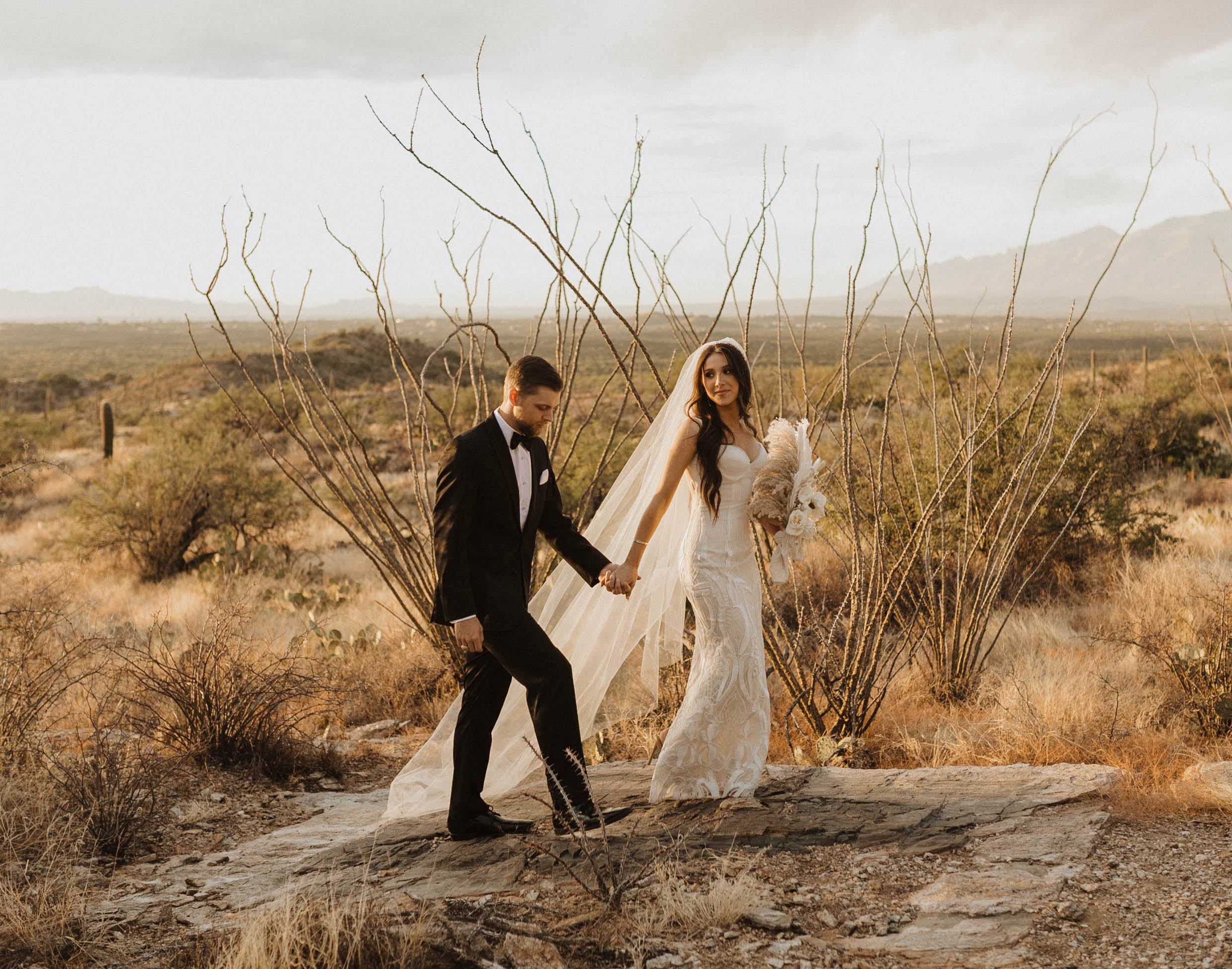 A bride and groom hold hands walking outside in Arizona's Saguaro National Park.