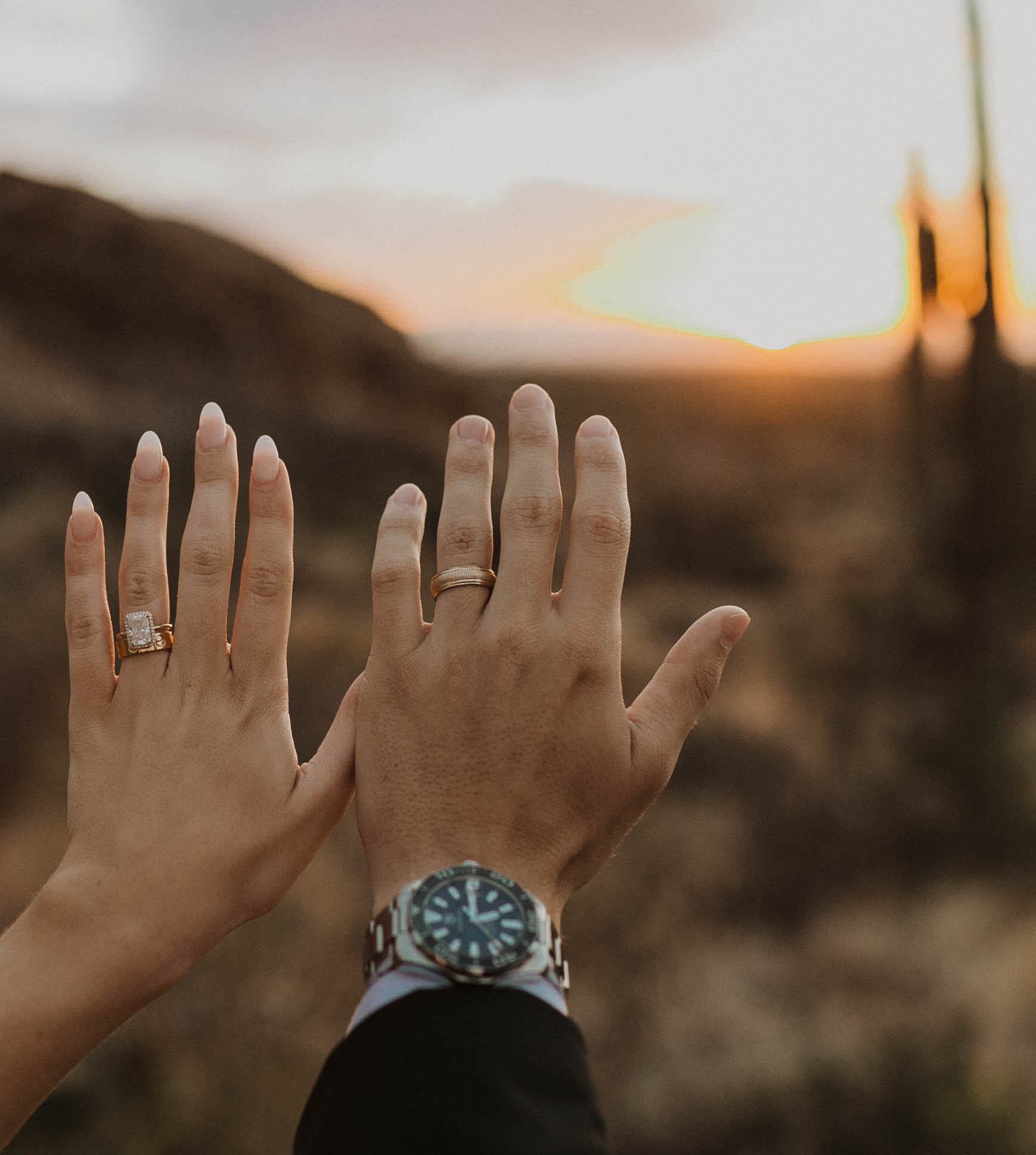 The bride and groom show off their wedding rings with a desert sunset in Arizona in the back.