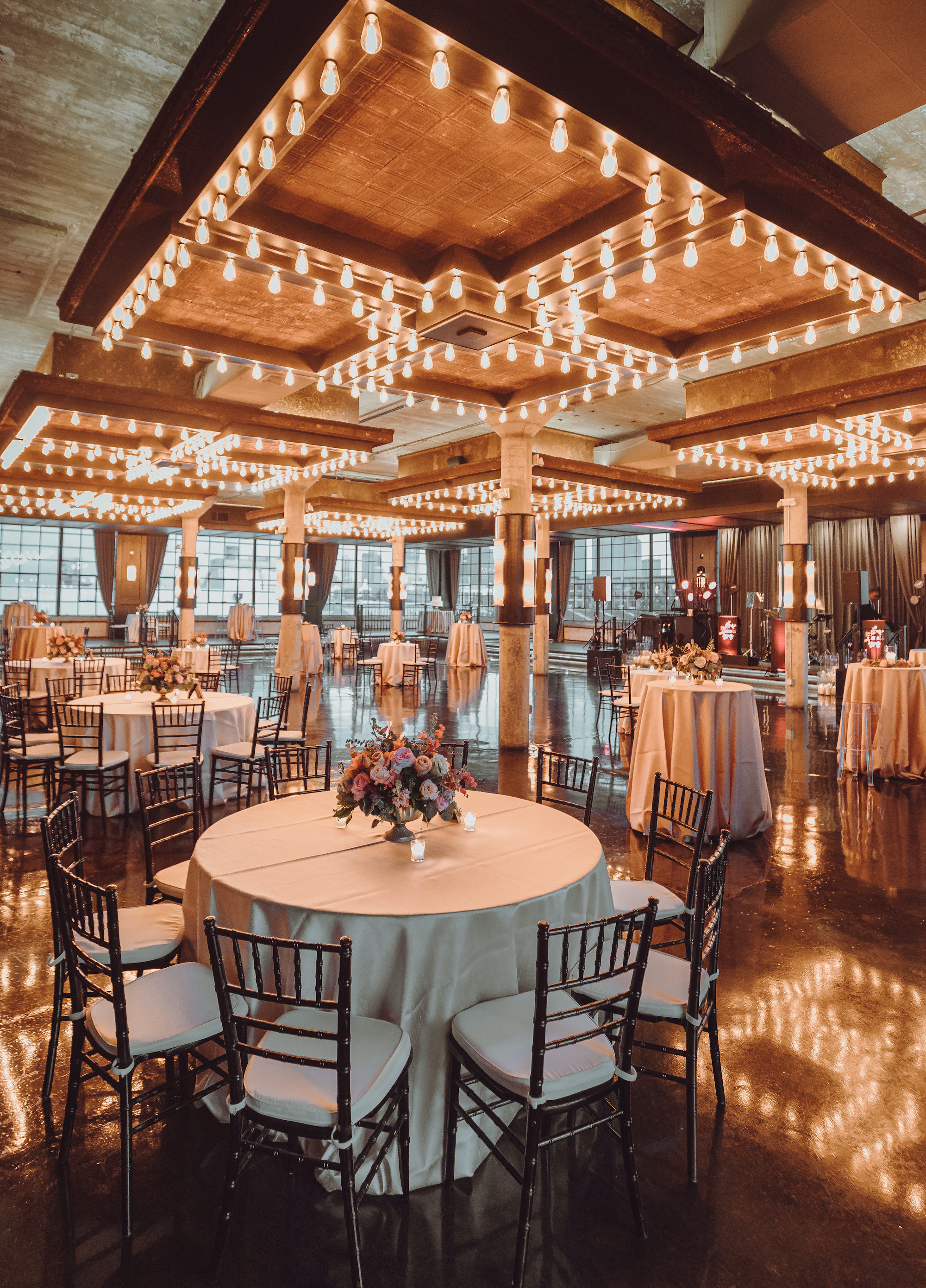 Round banquet tables with ivory linens topped with lit candles and small floral bouquets inside of the ballroom at The Astorian wedding venue.