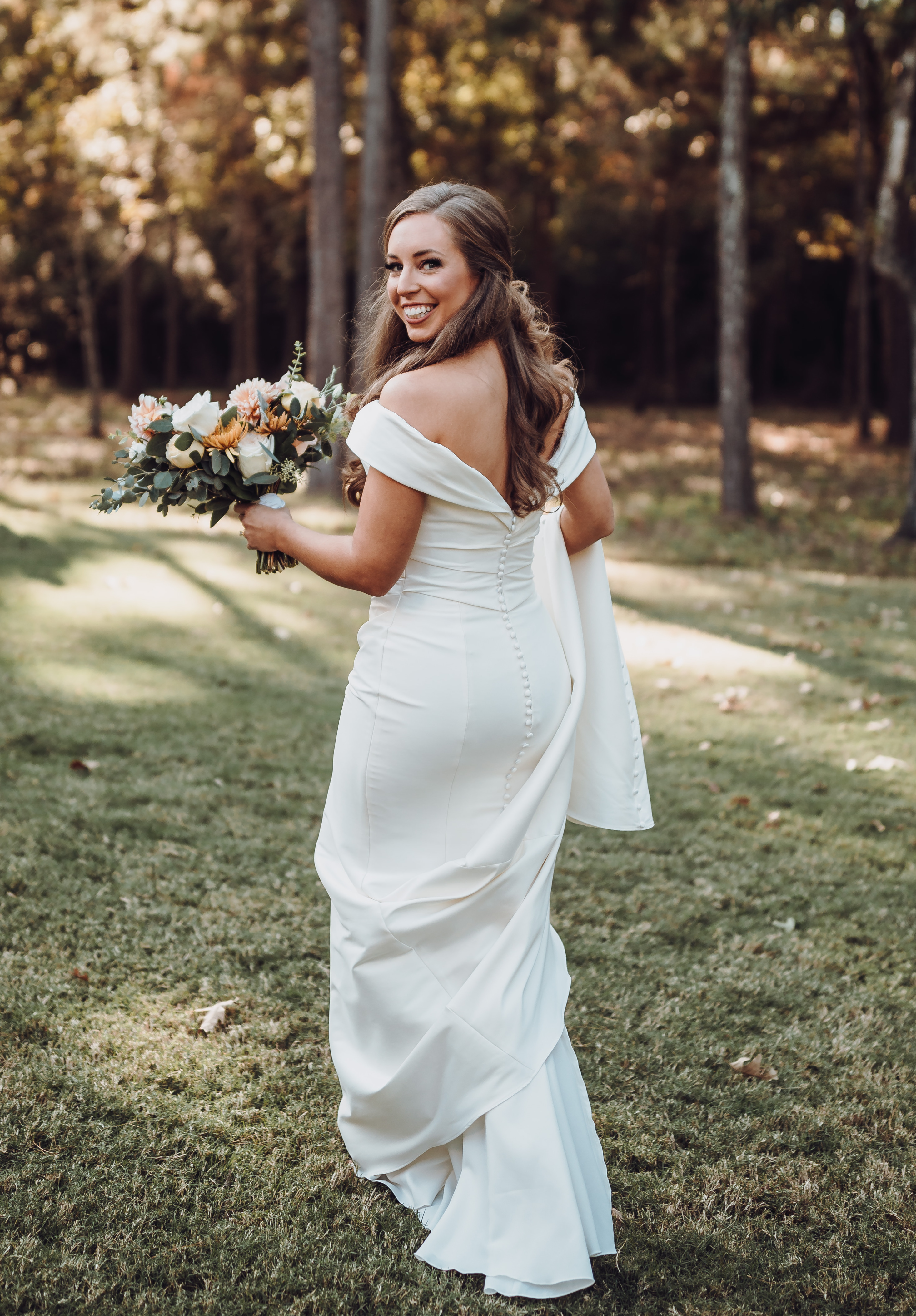 A bride holds her train and walks outside with her bridal bouquet in her other hand.