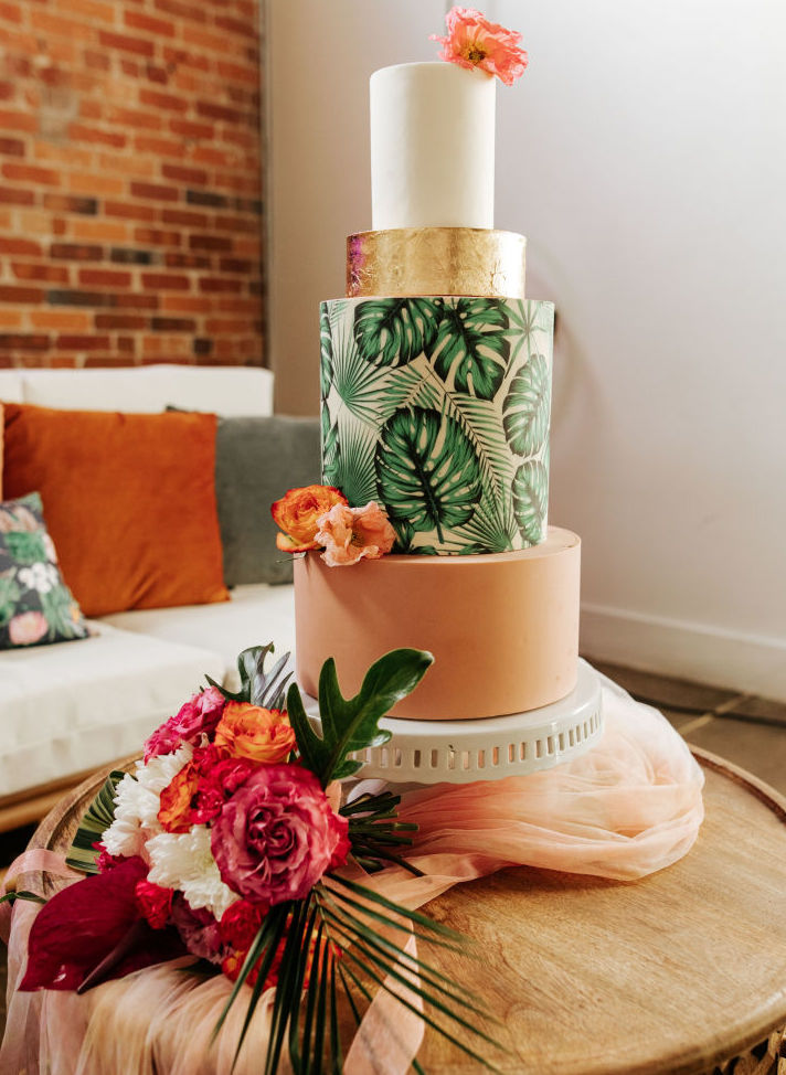 A tropical wedding cake with a palm design and peach, gold and white tiers with poppy flowers and roses.