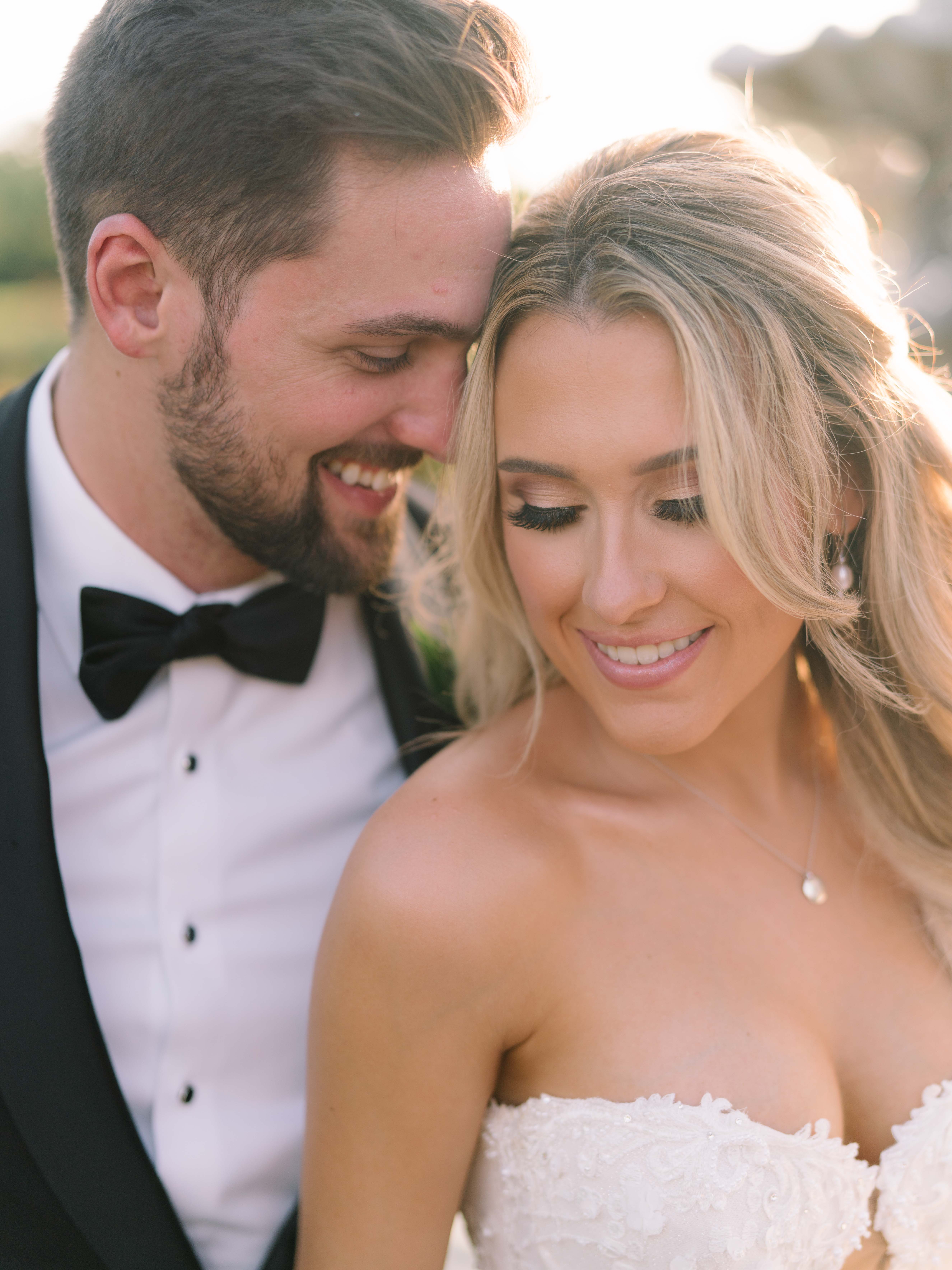 A bride and smile at each other outside with the sun beaming down on them.