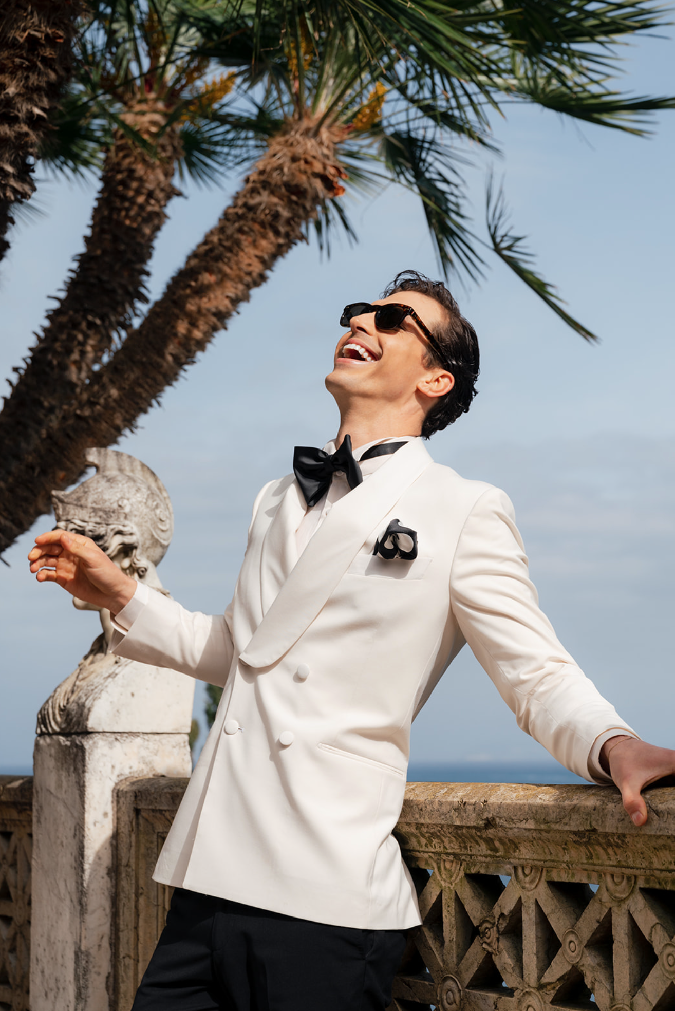 A groom laughs and waits outside for his bride and stands on a balcony overlooking the ocean on the Amalfi Coast in Italy.