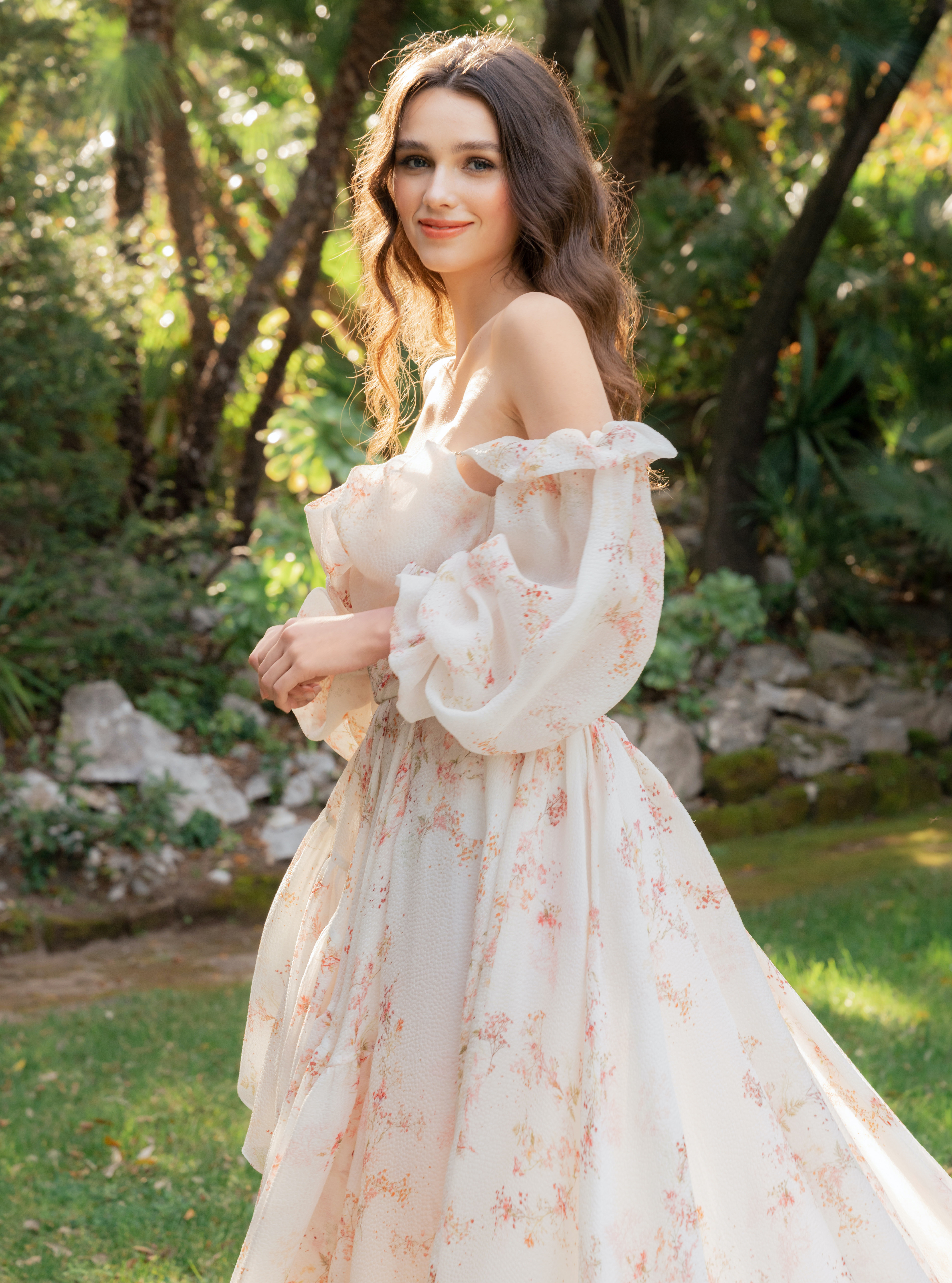 A bride soft smiles with a flowy off-the-shoulder Monique Lhuillier gown on in a lush garden of greenery in Italy.