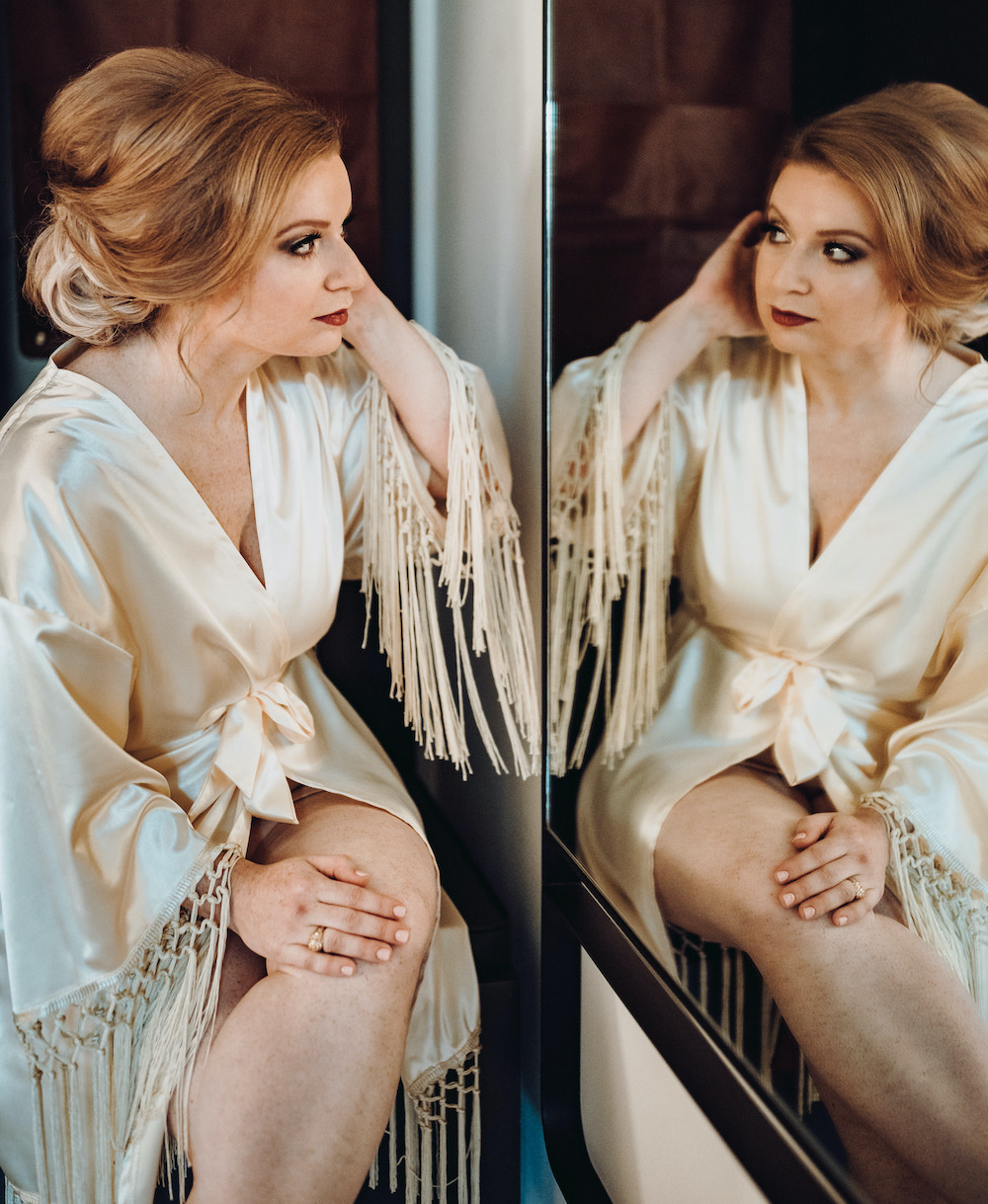 A bride has her hair and makeup done for her modern music hall wedding and looks at her reflection in a mirror.