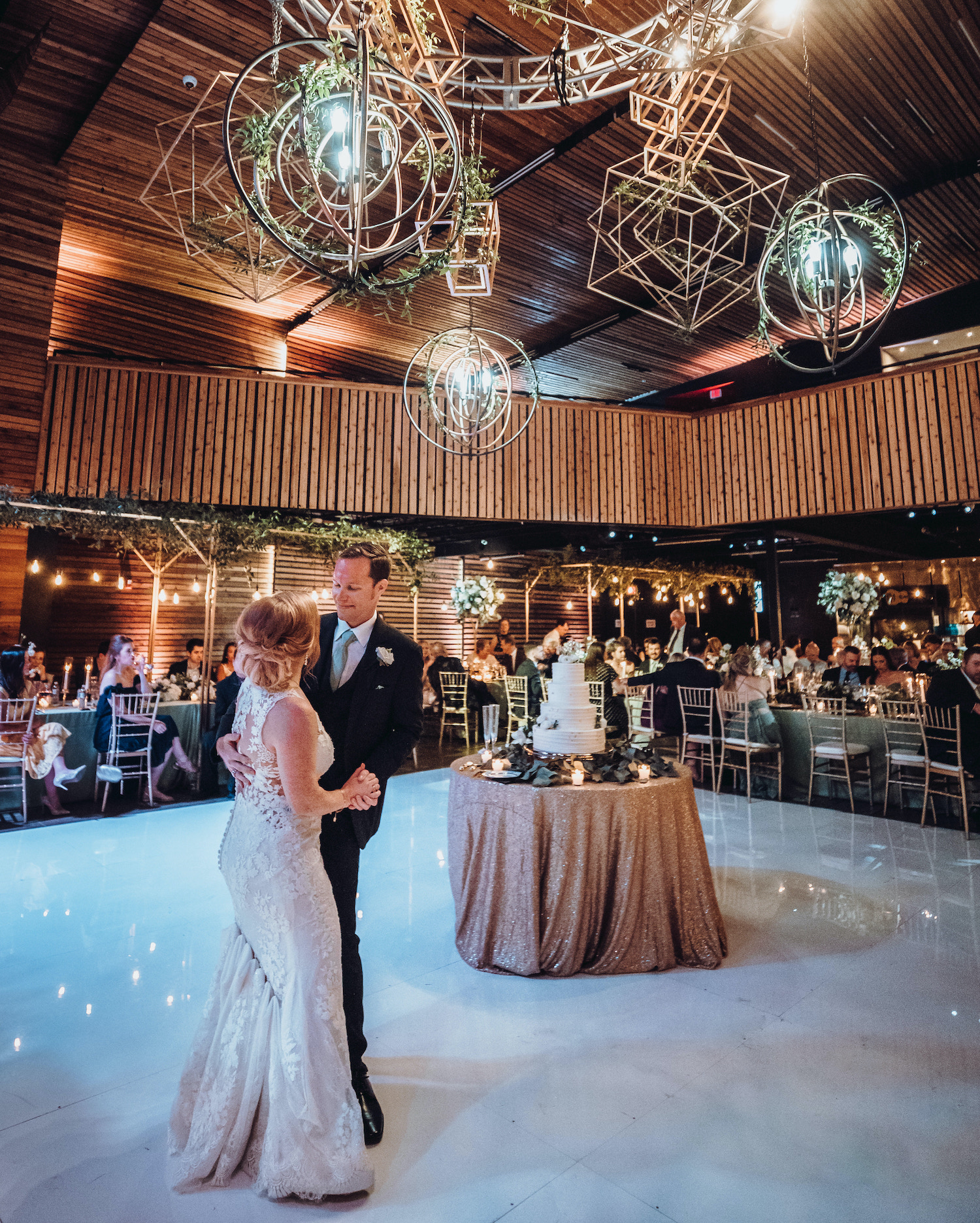 A bride and groom dance on the dance floor while their wedding guests watch them.