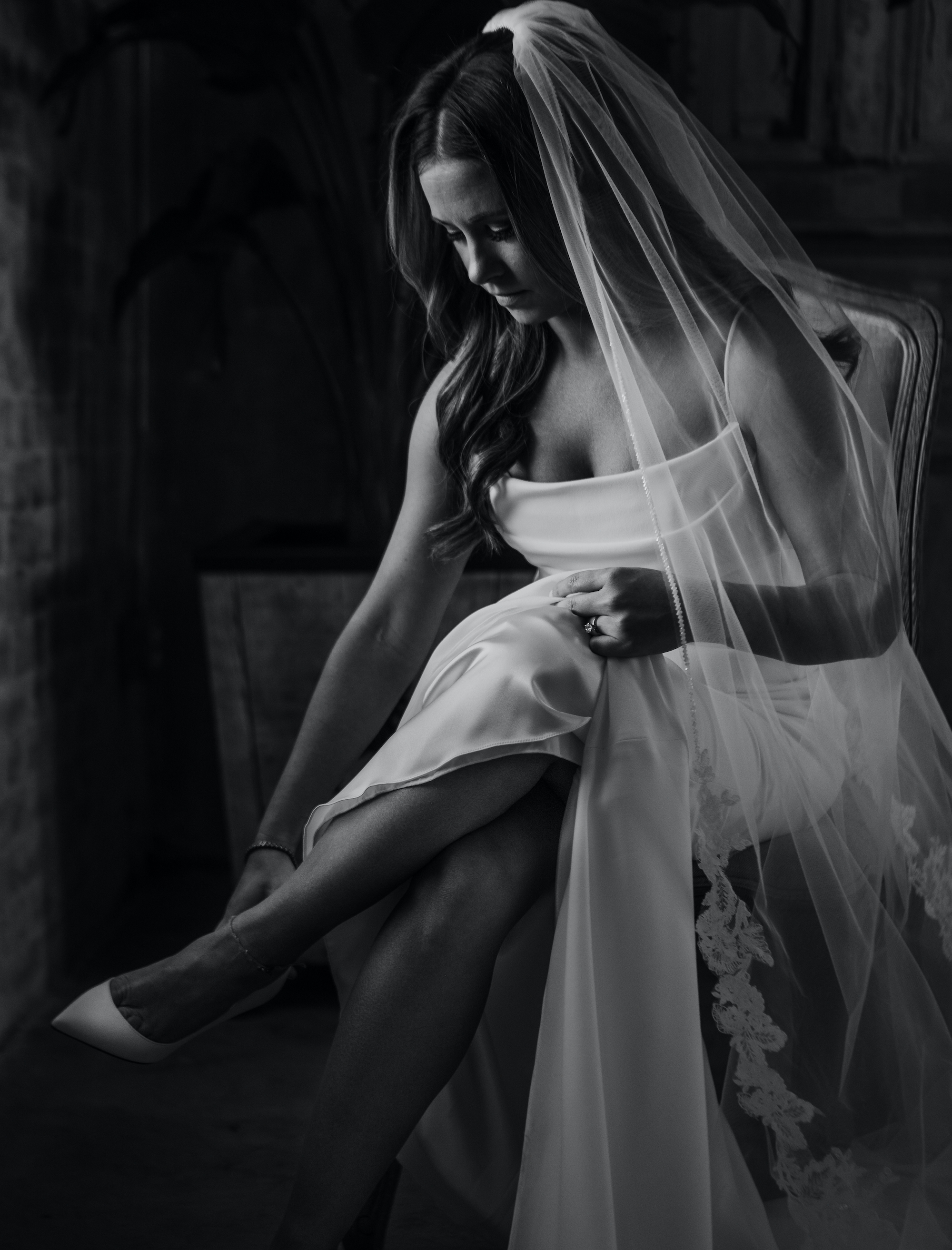 A black and white photo of a bride putting on her wedding shoes before her Jewel Toned Wedding With Art Deco Vibes.