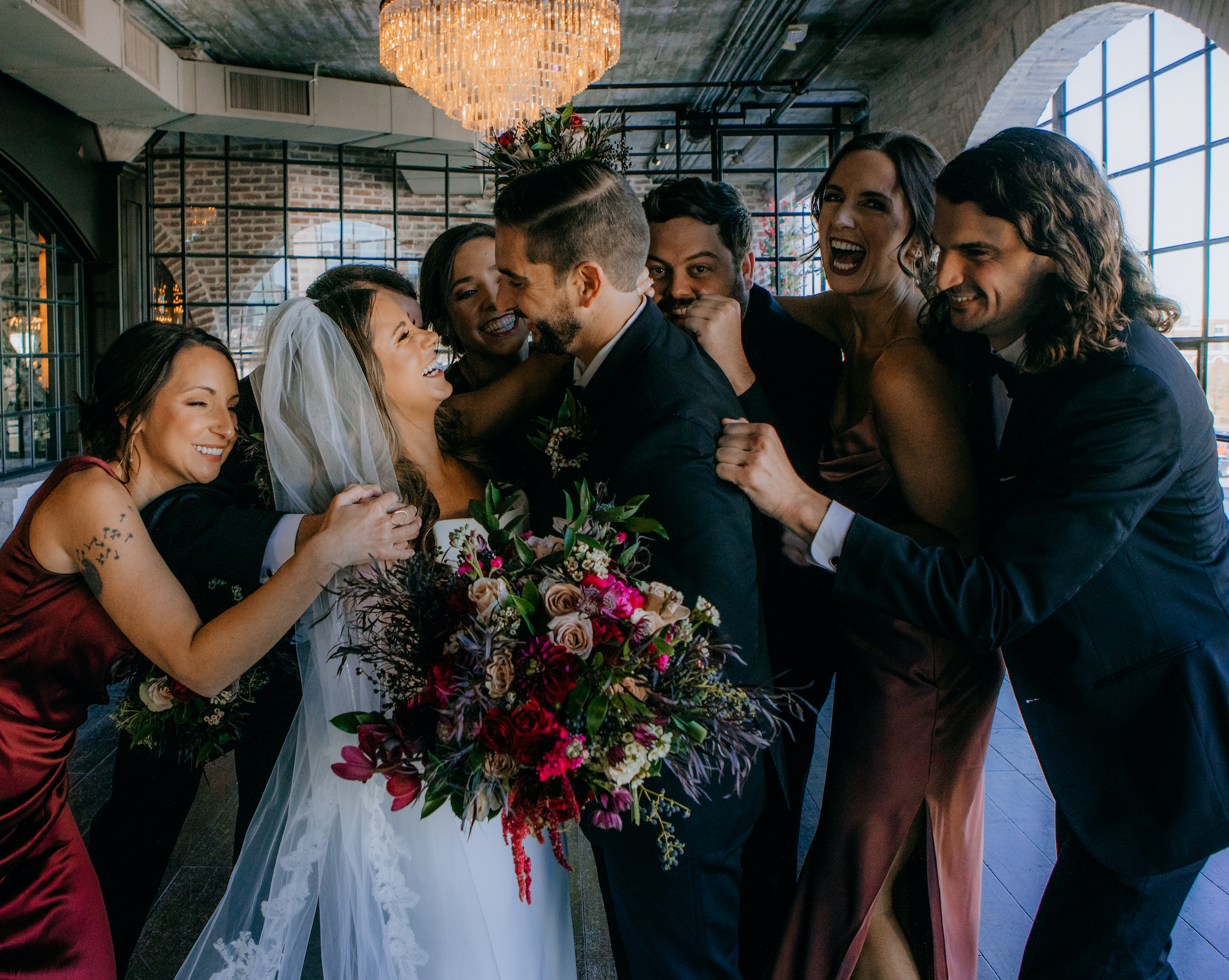 A bride and groom laugh while their friends stand behind them smiling.