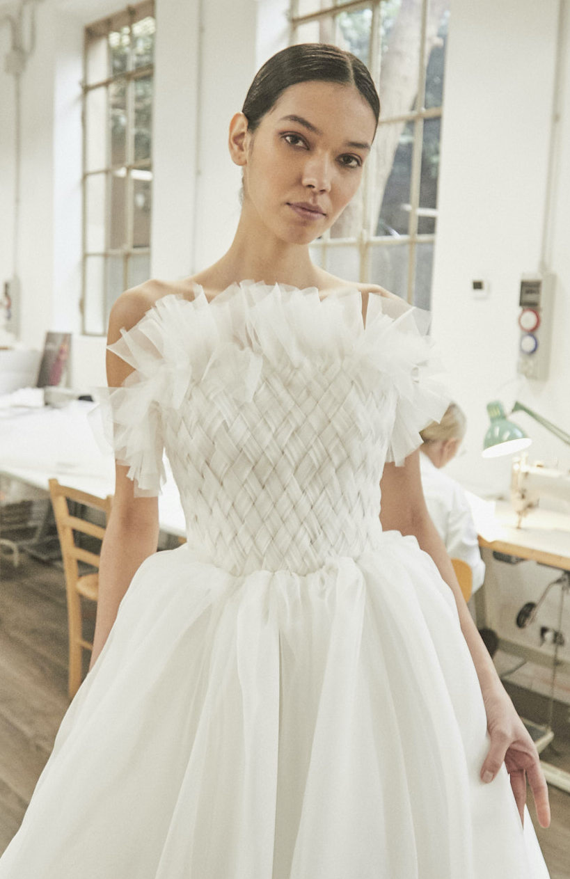 A model wears a Peter Langner wedding gown with a lace flower skirt and a halter neck style with extra silky fabric flowing down the side of the gown. wedding gowns for the spring and summer