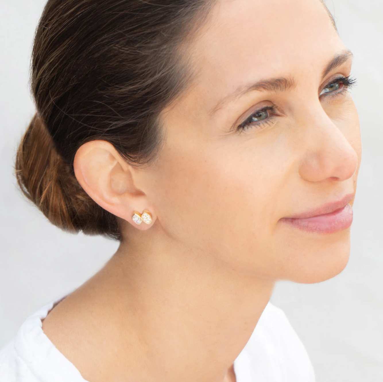 A brunette girl wears her hair in a bun so you can see one of her earrings designed by Erin Flynn Fine Jewelry.