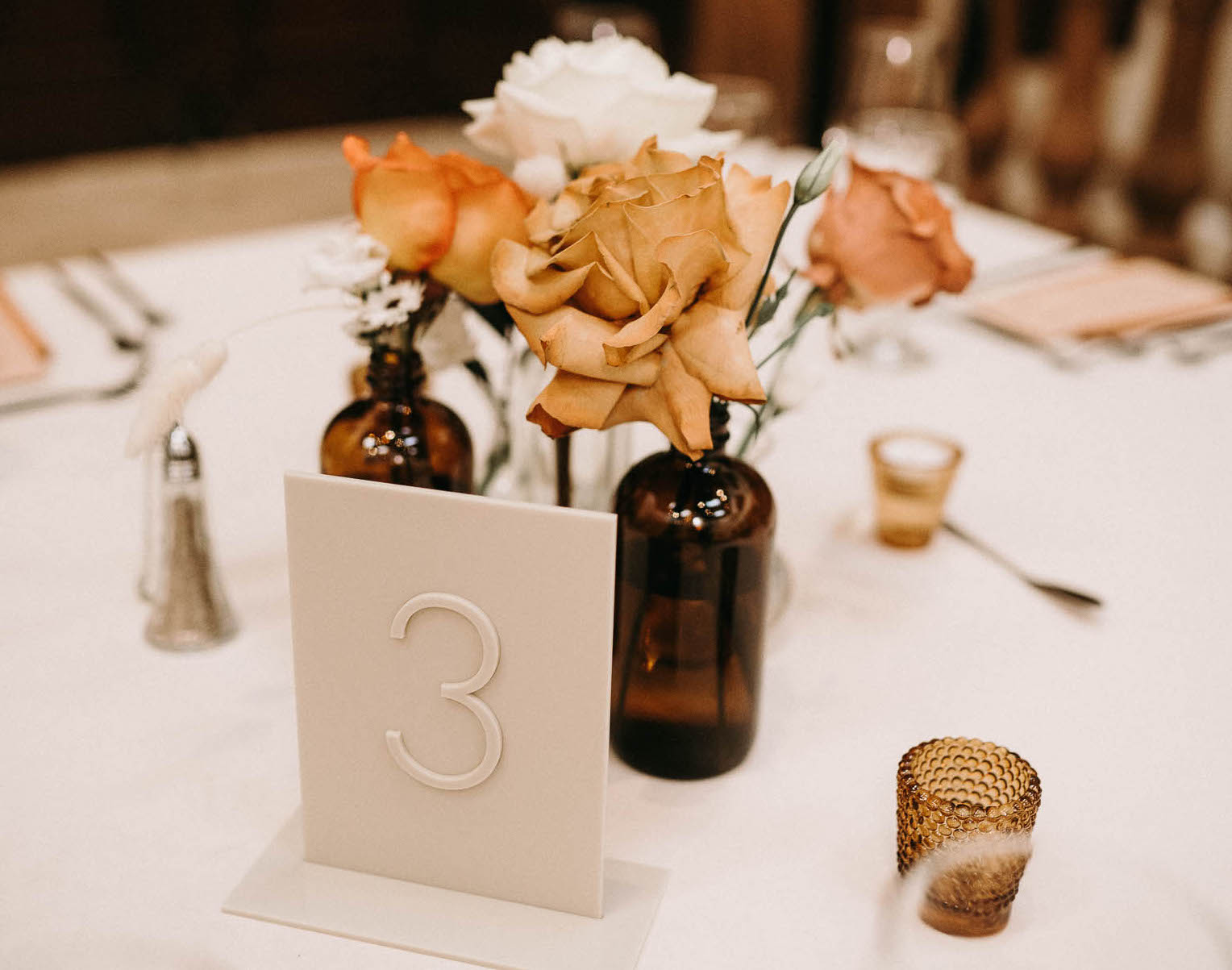 A wedding centerpiece with white and burnt orange flowers in bud vases for a wedding reception at The Bell Tower on 34th in Houston, TX.