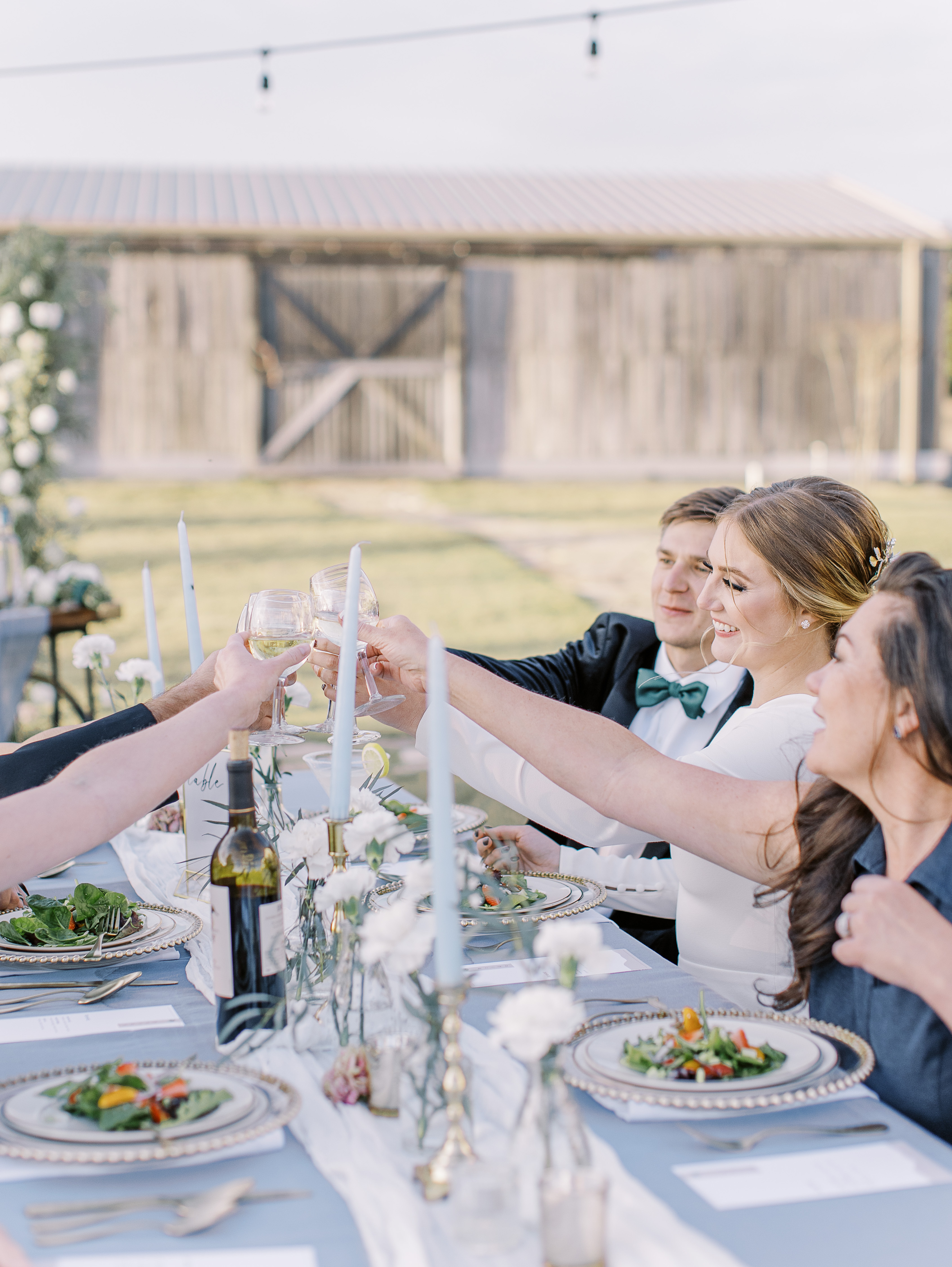 A bride and groom cheers their wedding guests at an alfresco dinner during their wedding reception.