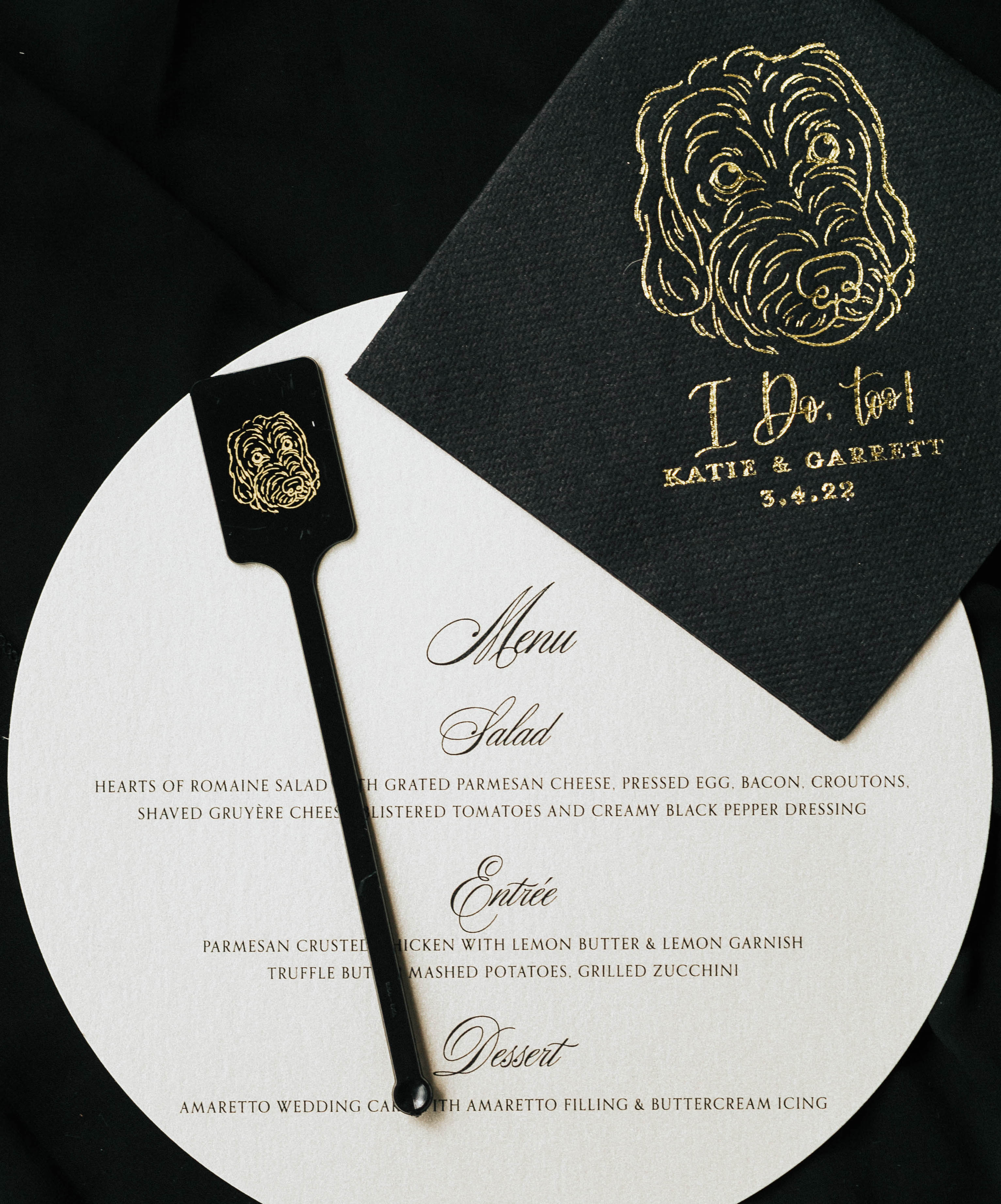 A gold, black and white invitation suite for a wedding that includes a menu and a cocktail napkin.