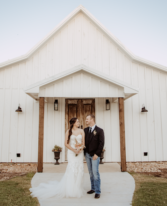 A bride and groom standing outside a white chapel.