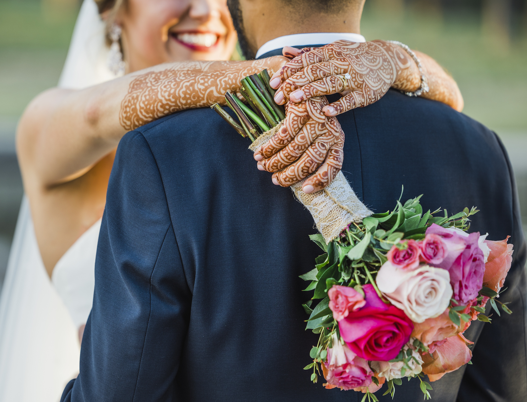 Bride wraps her arms around the grooms neck showing her henna tattoos. 