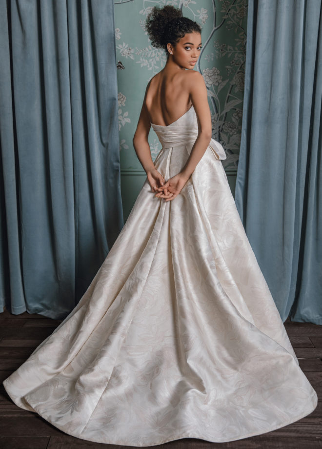 Woman in a strapless A-line gown of brushed floral jacquard with asymmetric bodice drape and full pleated skirt by Anne Barge