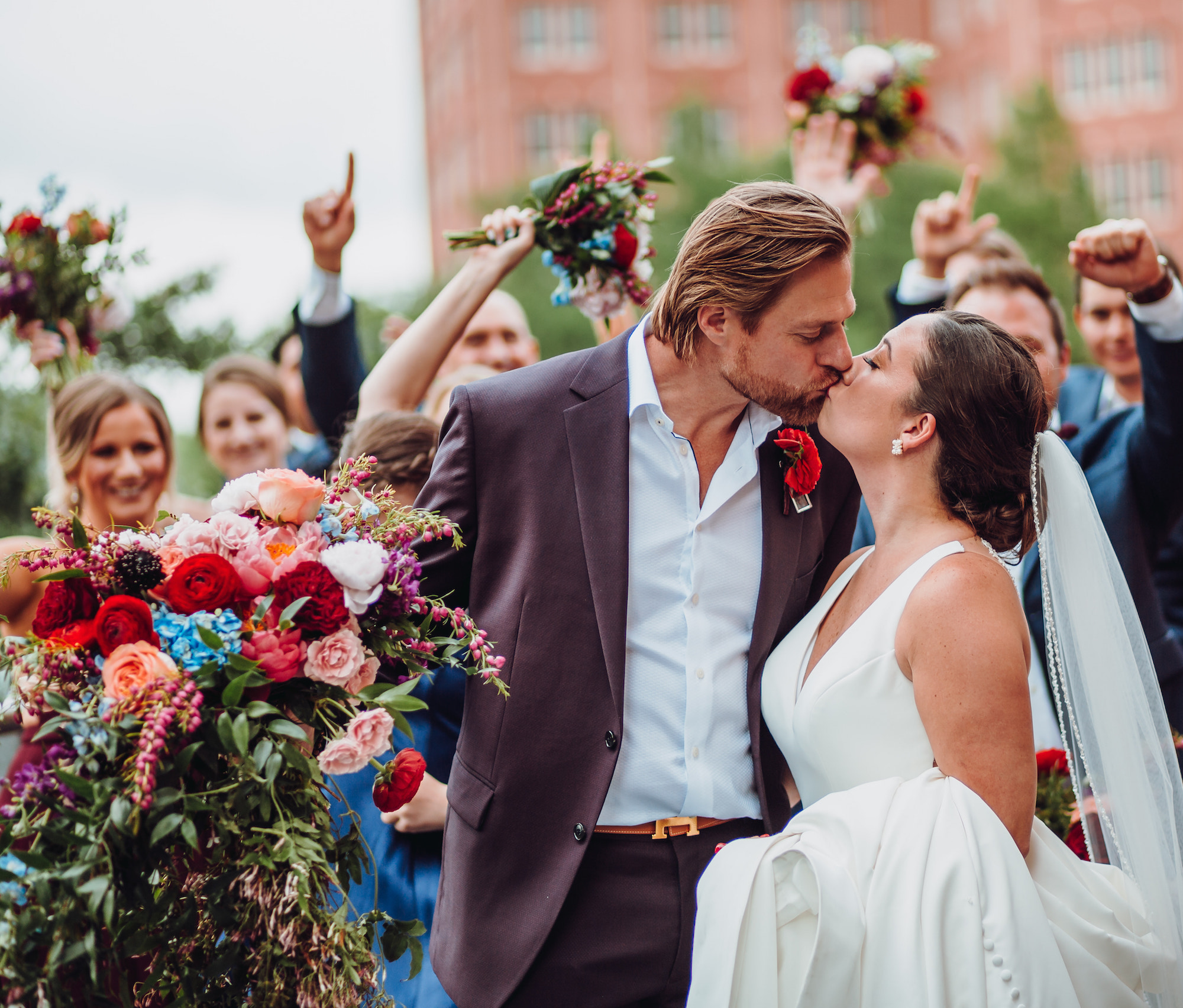 A bride and groom kiss outside while their wedding party cheers behind them during their whimsical tent wedding.