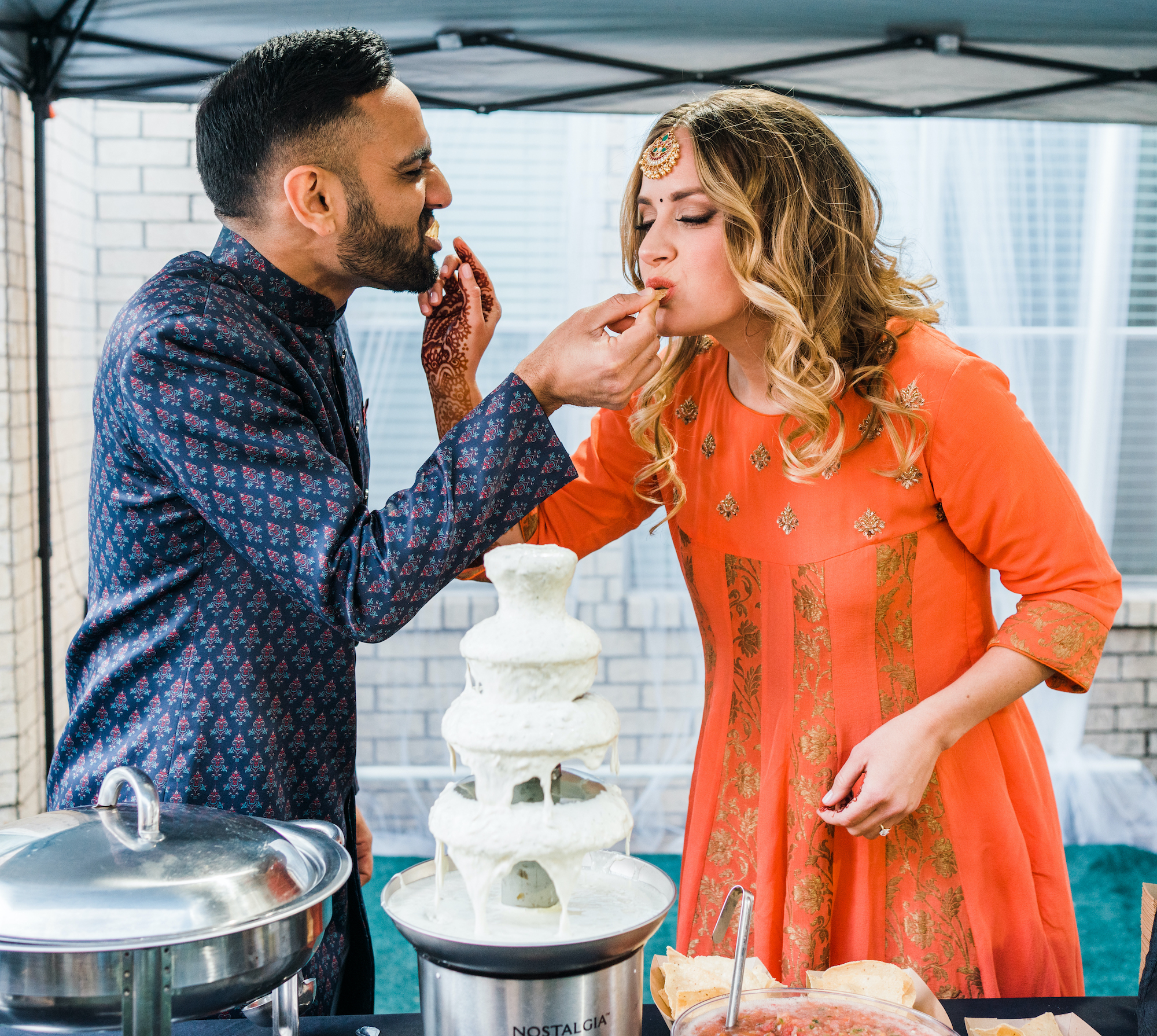 Bride and groom share a bite of chips and queso at their wedding celebration. 