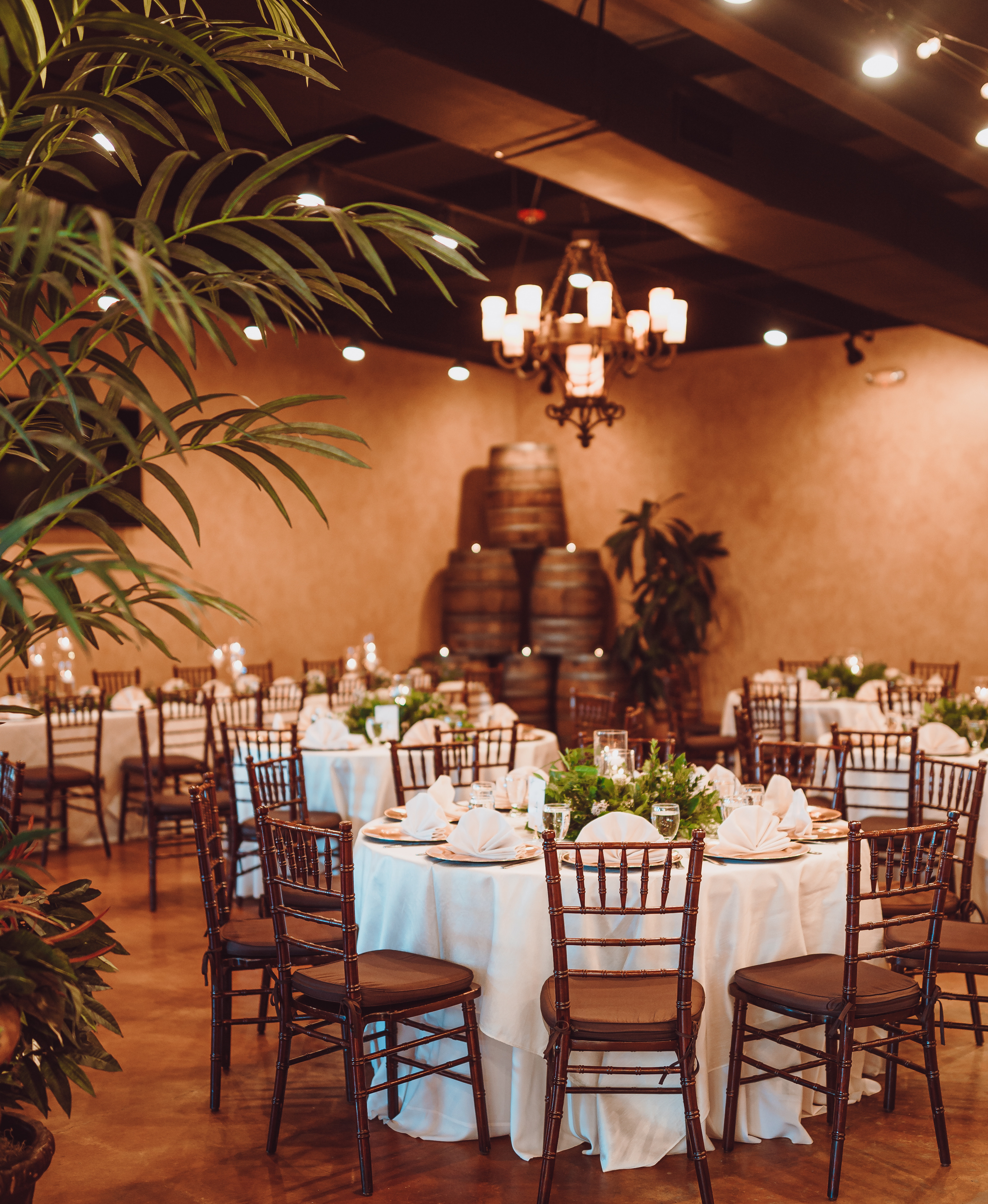 A reception room is decorated with palm trees and white accents along with candles.