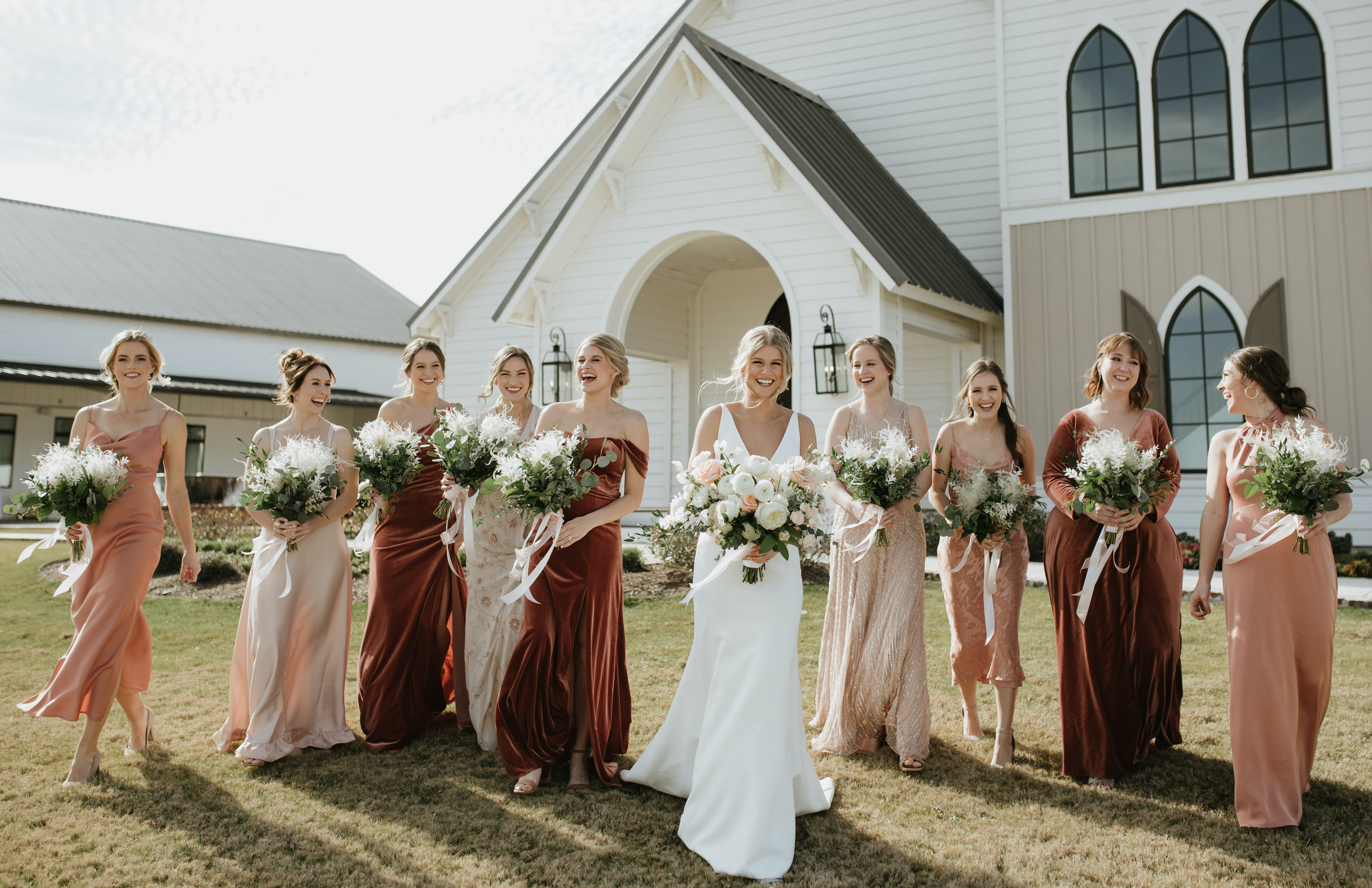 A bride smiles and walks with her bridesmaids outside before her peach-toned countryside wedding in Brenham, TX.