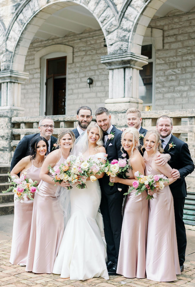 The bride and groom smile with their bridesmaids and groomsmen outside of the church after their wedding ceremony. 