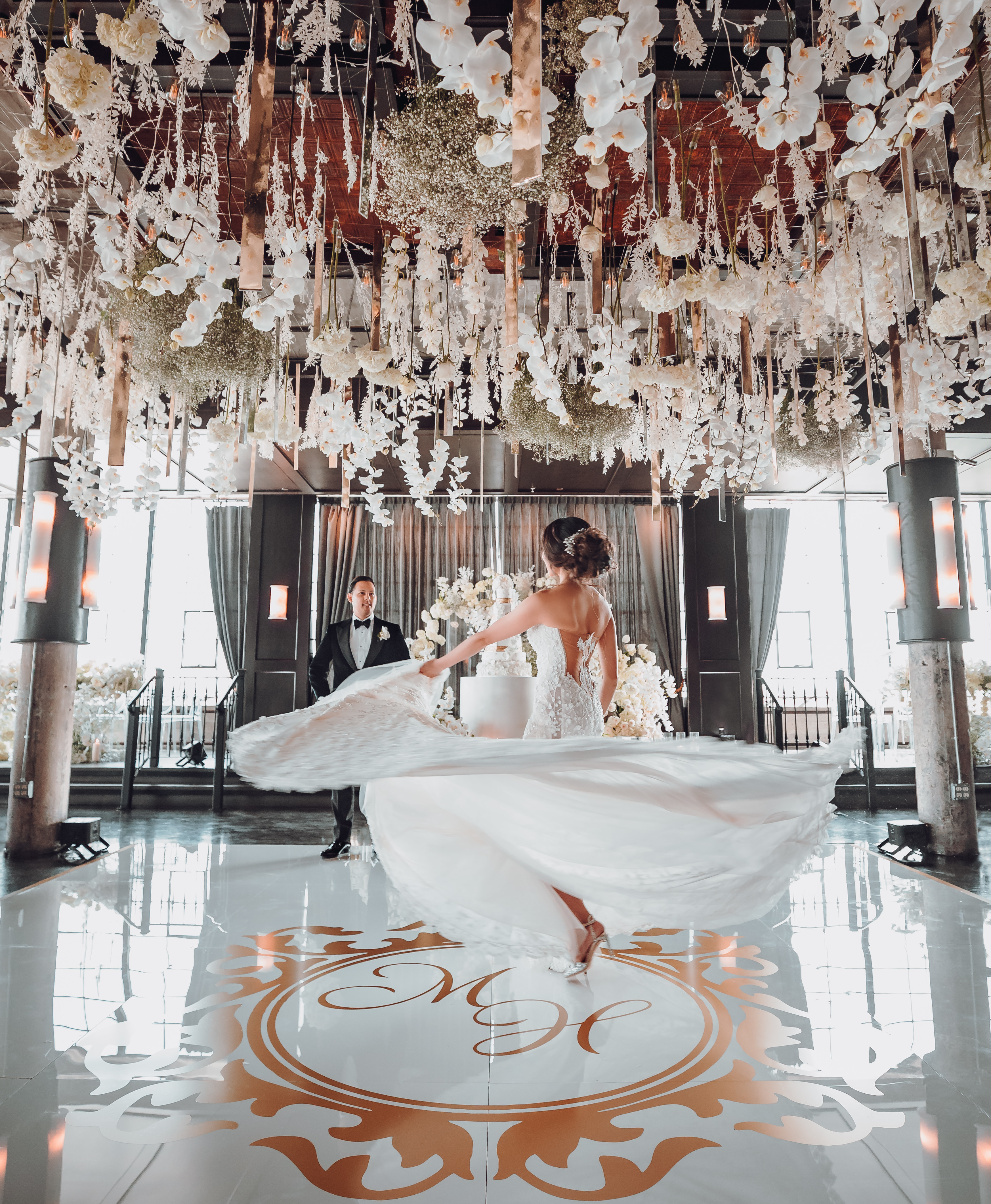 A bride and groom dance in their reception room under a canopy of white flowers and gold accents.