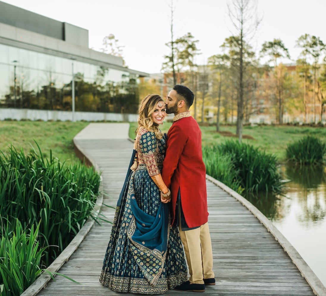 Groom in wedding kurta kisses a bride in a bridal saree on the evening of their sangeet at Marriott Cityplace at Springwoods Village. 