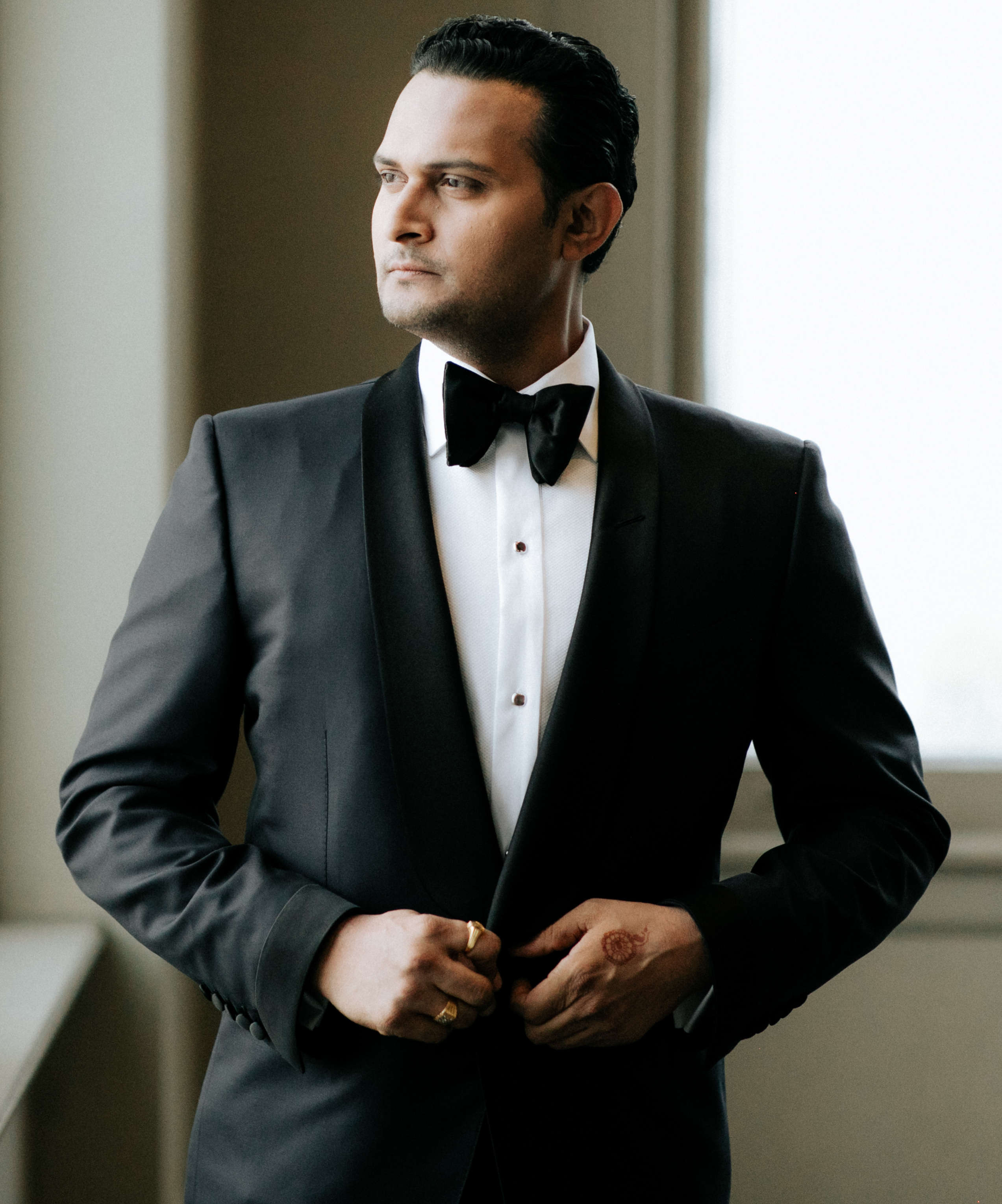 The groom buttons up his tuxedo as he gets ready. 