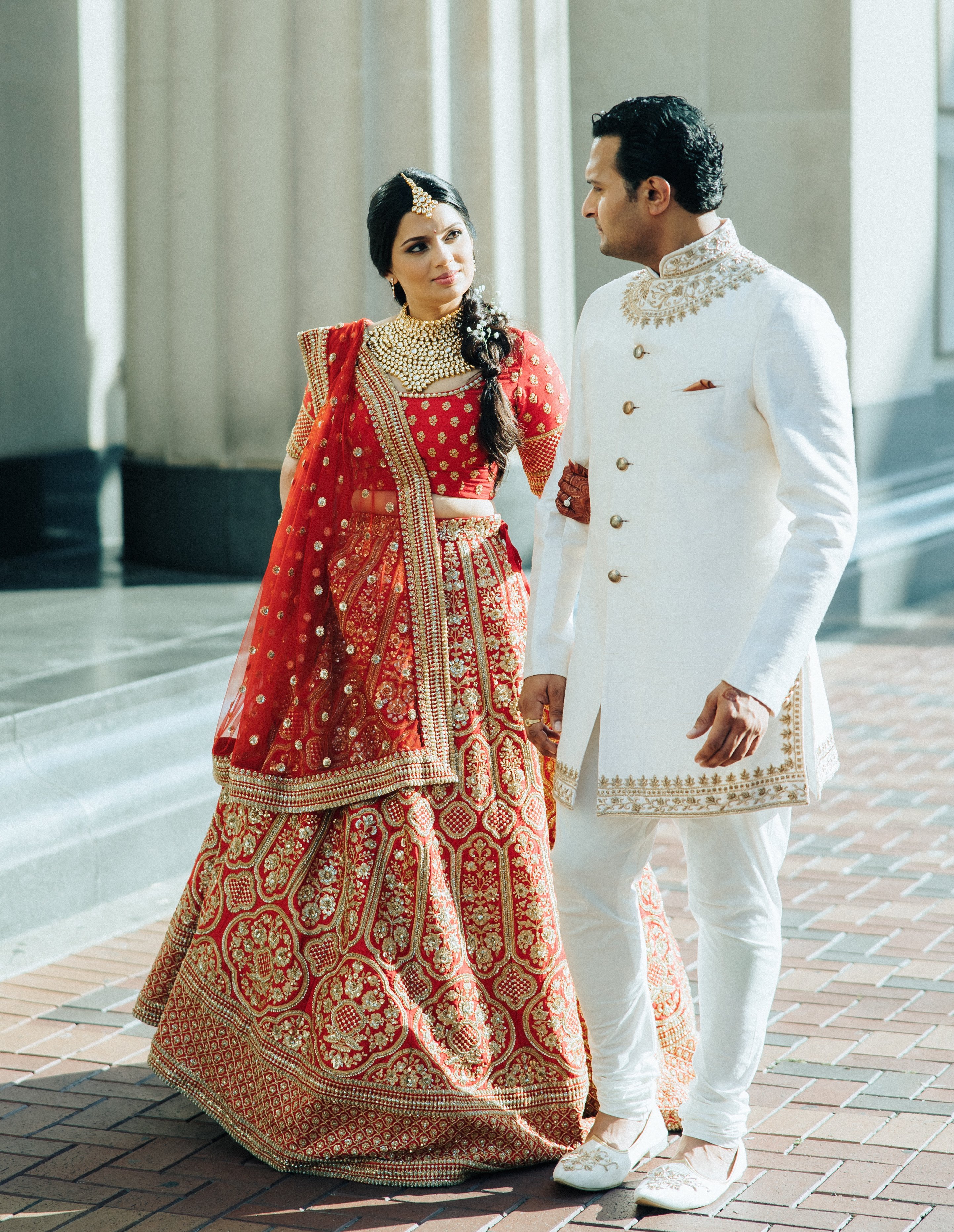 The bride and groom hold hands while dressed in traditional Hindu attire outside their wedding venue. 