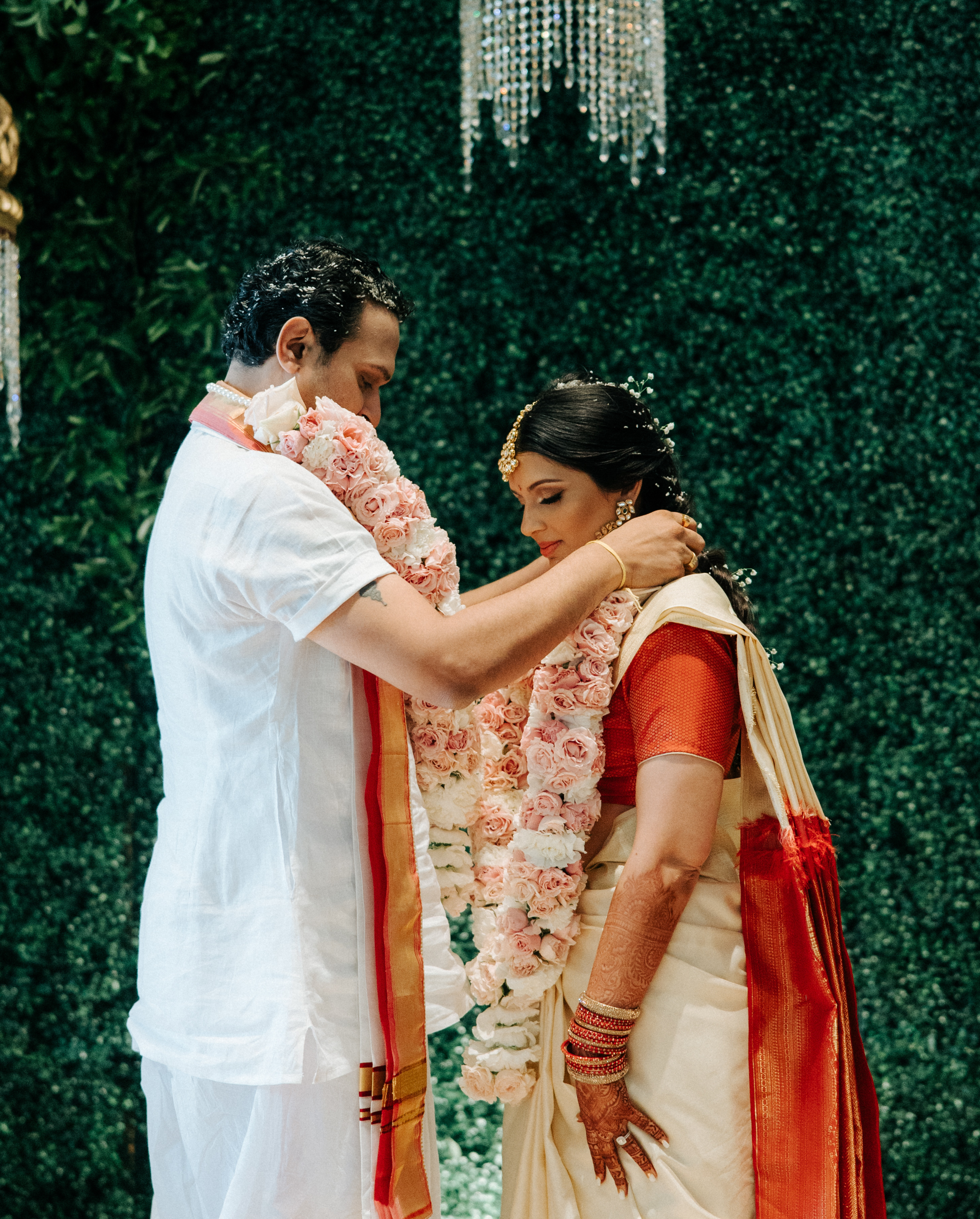 The bride and groom place white and peach floral necklaces around each others necks. 