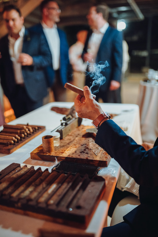 A guest holds a smoking cigar outside at the whimsical tent wedding in Downton Houston. 