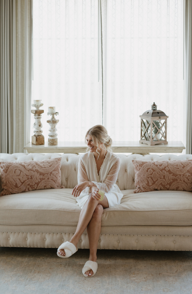 A bride sits on the couch while getting ready in the bridal suite at the Texas wedding venue, Deep In The Heart Farms. 