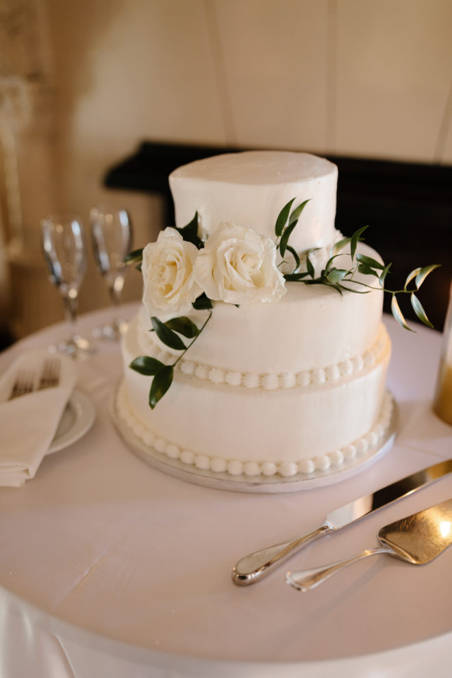 Small three tier white wedding cake with two roses on a cake table at a Sarasota Florida wedding. 