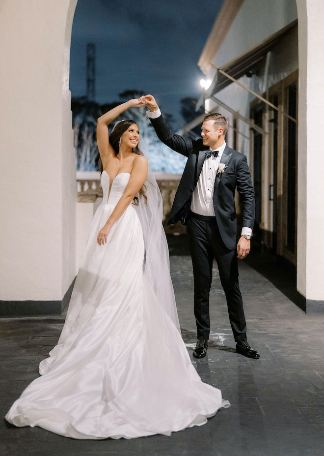 The bride and groom smile as they dance outside their wedding venue. 