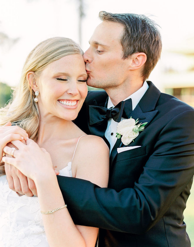 The groom kissing the brides forehead as she smiles.