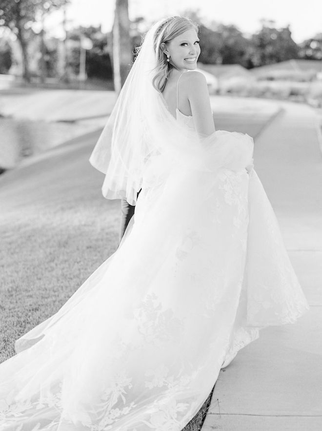 The bride looking back and smile as she holds up her Monique Lhuillier gown.