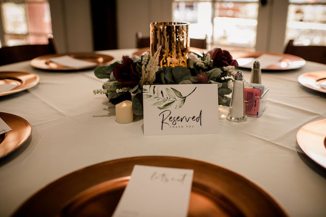 A card on the reception table reading "Reserved thank you" with gold chargers and a red rose centerpiece arrangement.