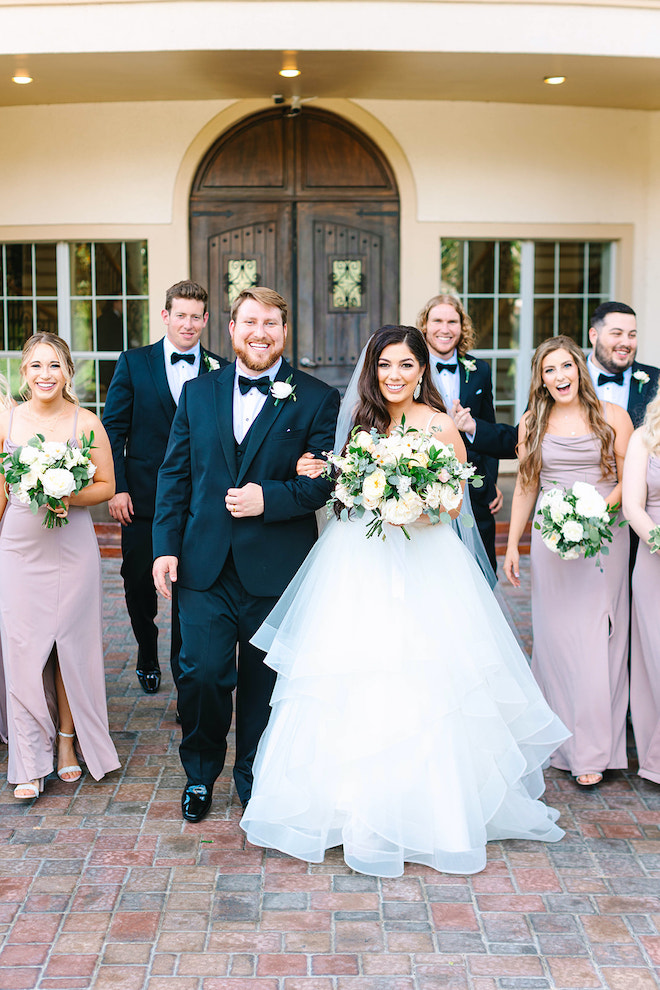 The bride and groom walking out of the ceremony with their wedding party following behind them.