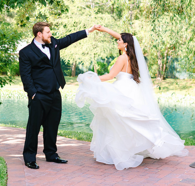 The groom spinning the bride with trees and a pond behind them.