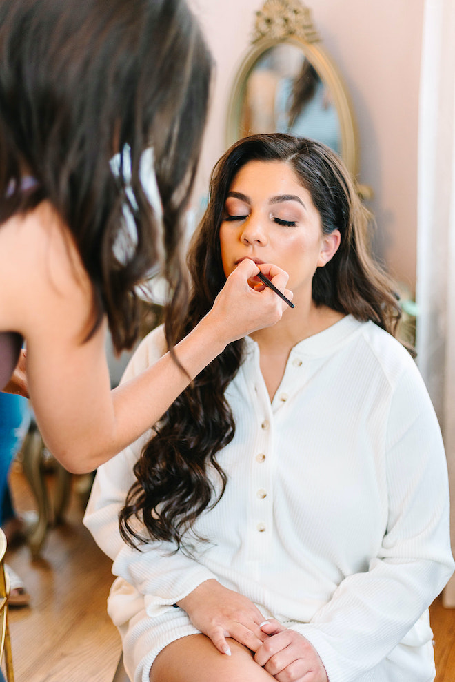 The bride getting lipstick applied by a makeup artist. 