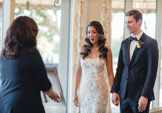 bride and groom look at a painting made for them by Rendered Moments, at a vow renewal planned by Mari + Jess Designs at Pine Forest Country Club in Houston, TX