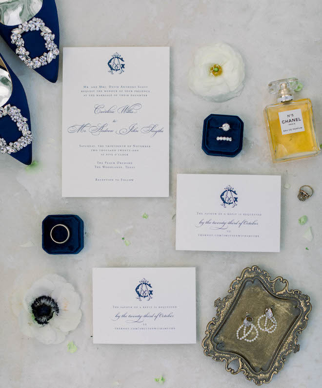 The wedding invitations surrounded by the rings, earrings, Chanel perfume, and the bride's blue shoes.