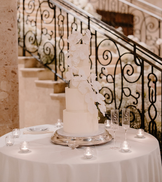 A four tier white wedding cake decorated with orchids at a white, black and black reception at The Bell Tower on 34th in Houston. 