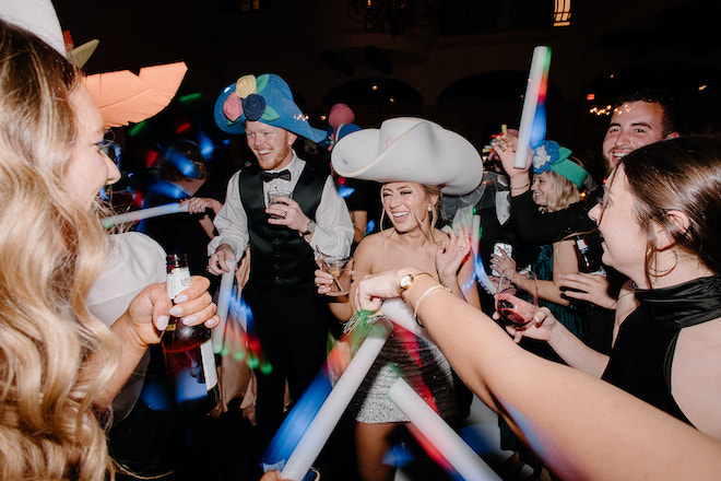 Groom and bride wear oversized novelty hats at their black, white and blush reception. 