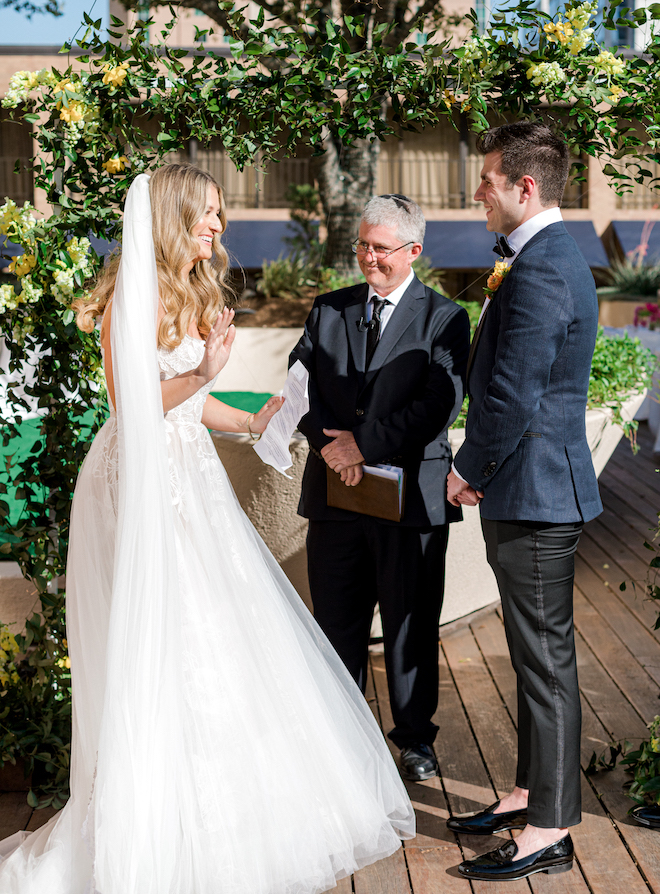 The bride smiling as she reads her personalized vows to the groom at the altar.