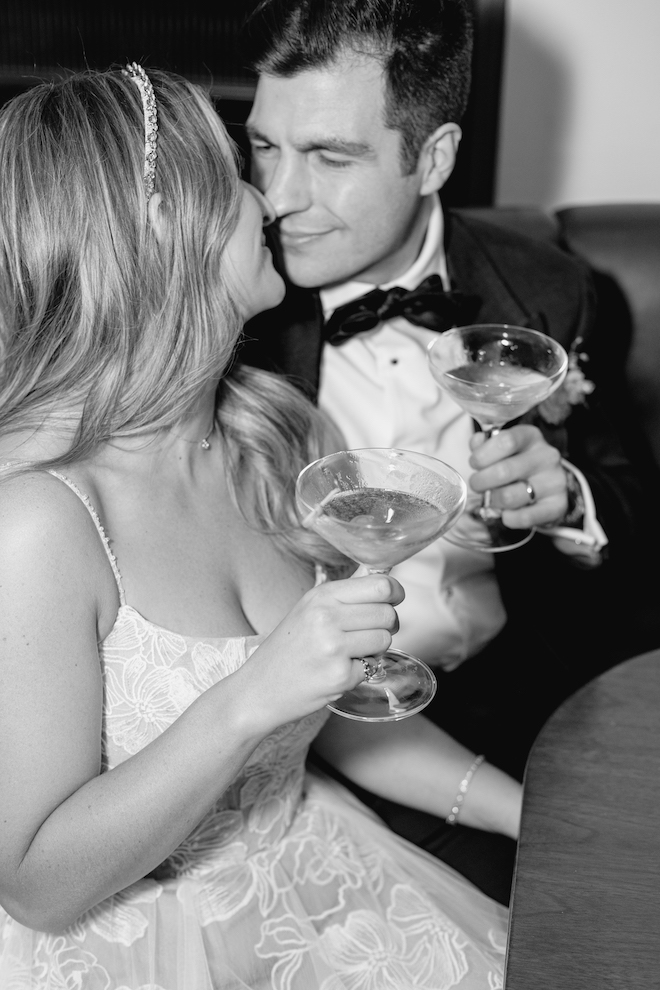 The bride and groom smiling at each other as they both hold cocktails in the Four Seasons Hotel Houston lounge during their colorful spring wedding.